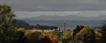 Fall trees in red, orange and green above Lake Champlain with mountains across the water