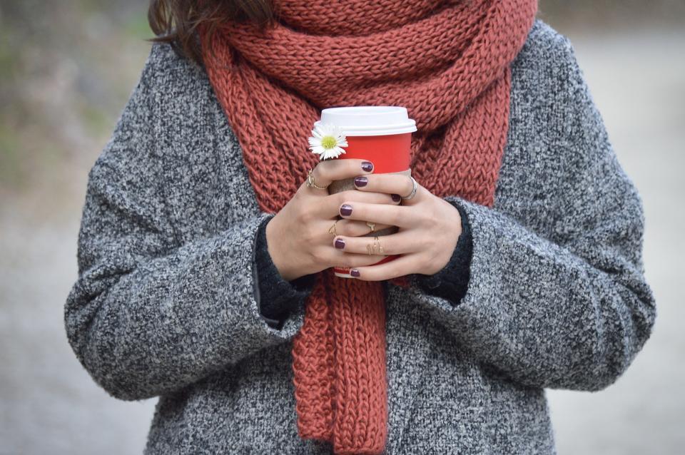 Woman wearing a knit scarf and coat holding a takeaway coffee cup